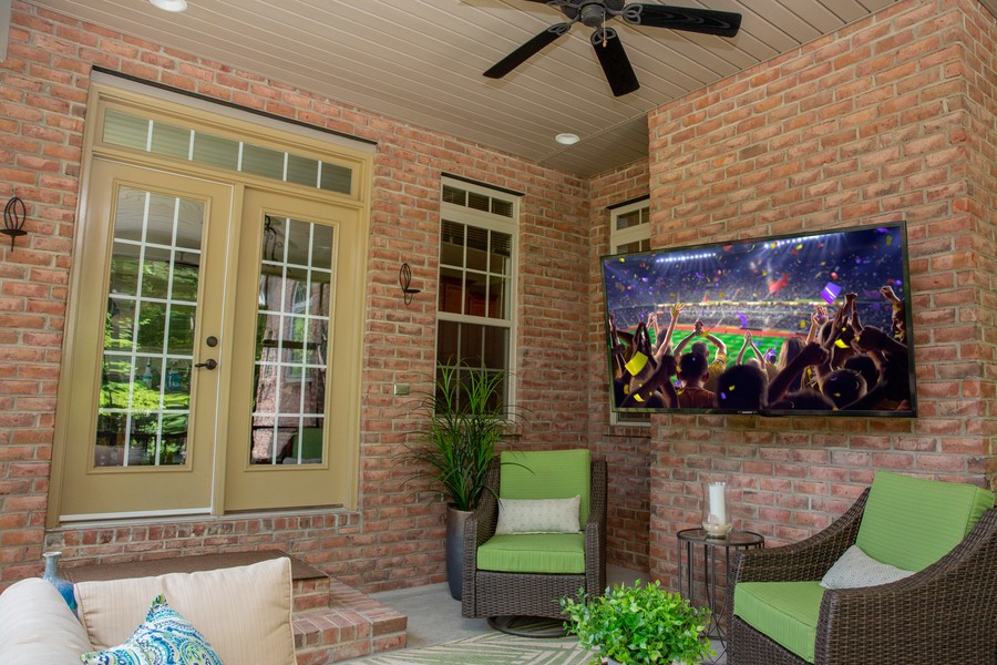 A patio with an outdoor TV mounted on a brick wall. 