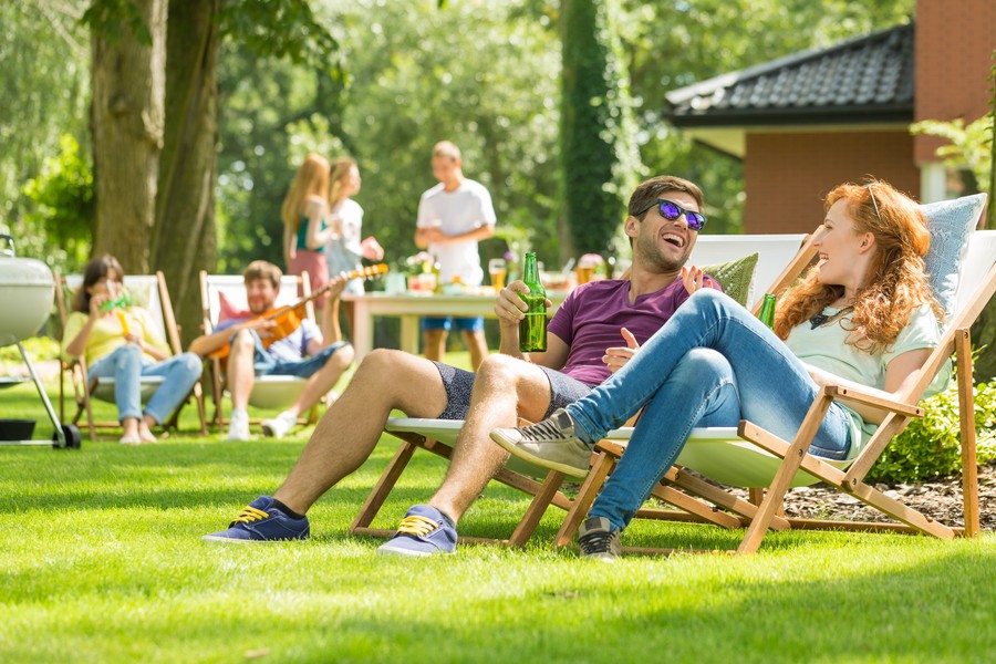 Couple walking on the green grass in their backyard with Klipsch speakers nestled in the foliage. 