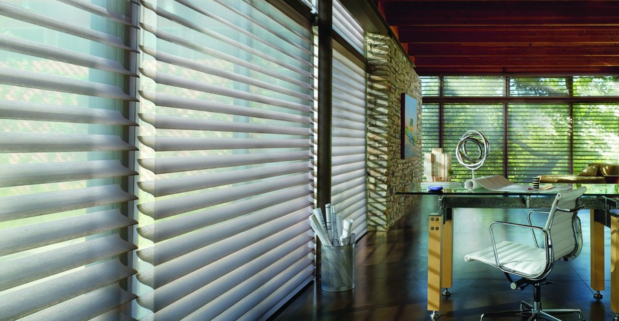 Hunter Douglas shades partially open along floor-to-ceiling windows in an office with a desk, chair, and drawings.