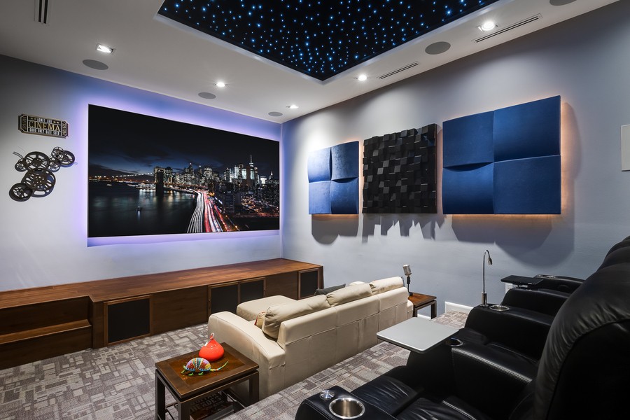 Home theater space with tiered seating, acoustic panels on the wall, and a road scene showing on the big screen TV.
